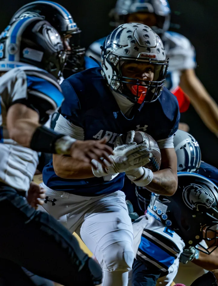 A football player carries the ball as defenders close in around him.