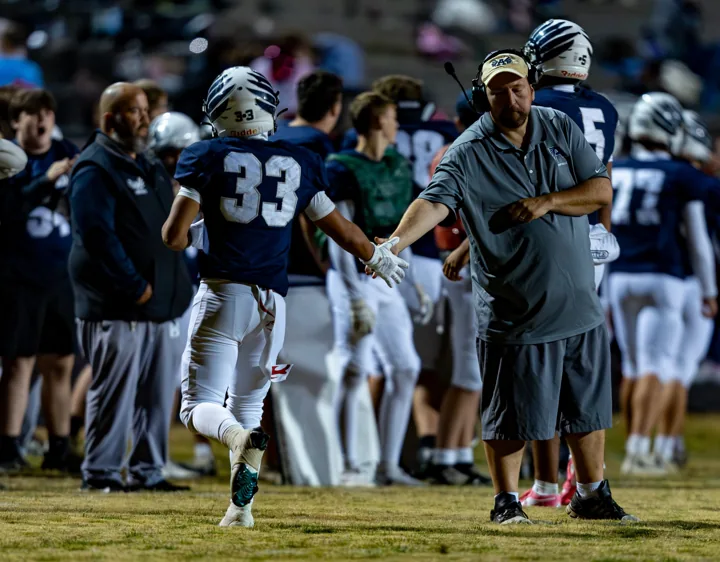 A football player wearing number 33 runs past his coach toward the sideline.