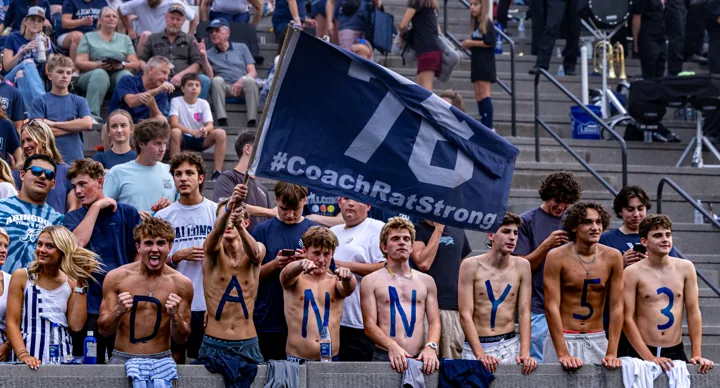A student section stands behind a banner and cheers from the grandstand.