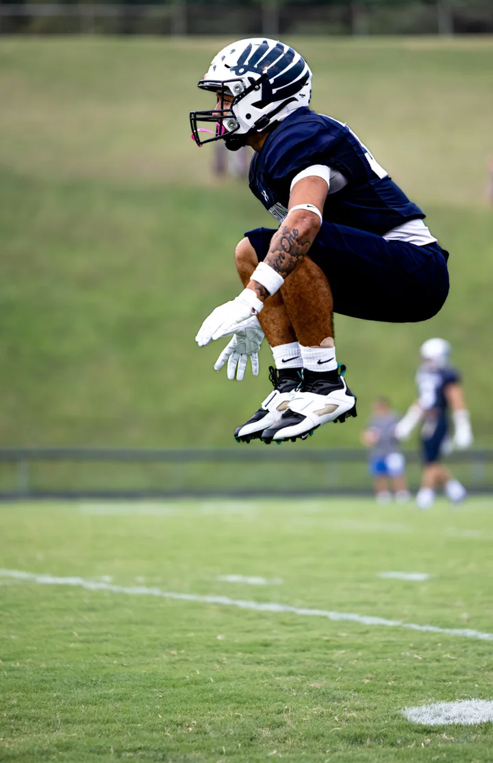 A helmeted football player jumps high during warm-ups on the field.