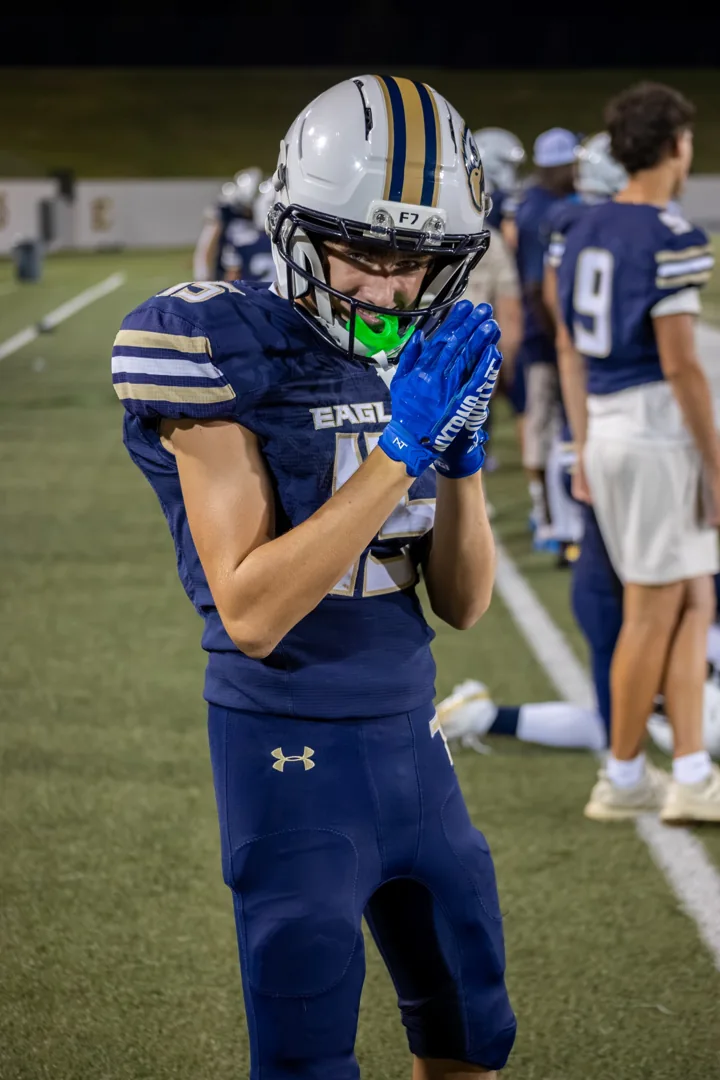 A football player adjusts a bright green mouthguard on the sideline.