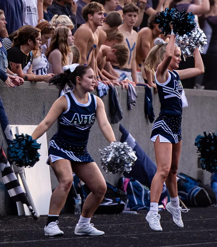 Cheerleaders perform near the track in front of the football stands.
