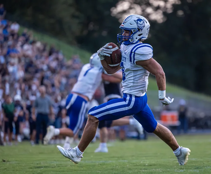 A football player carries the ball at full stride across the field.