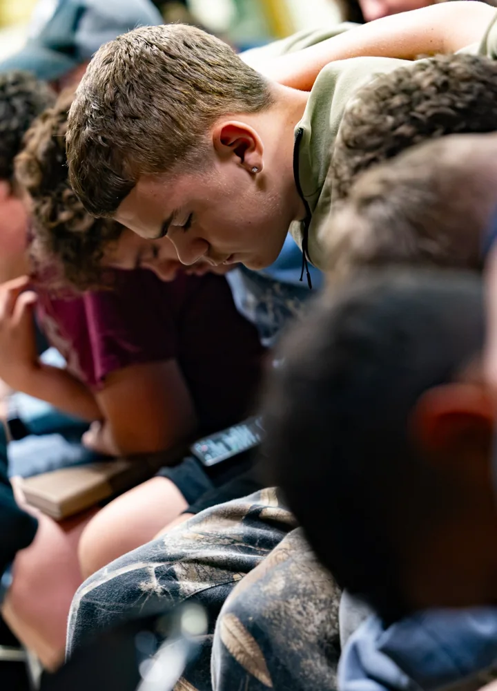 Young people lean forward over open books during a group gathering.