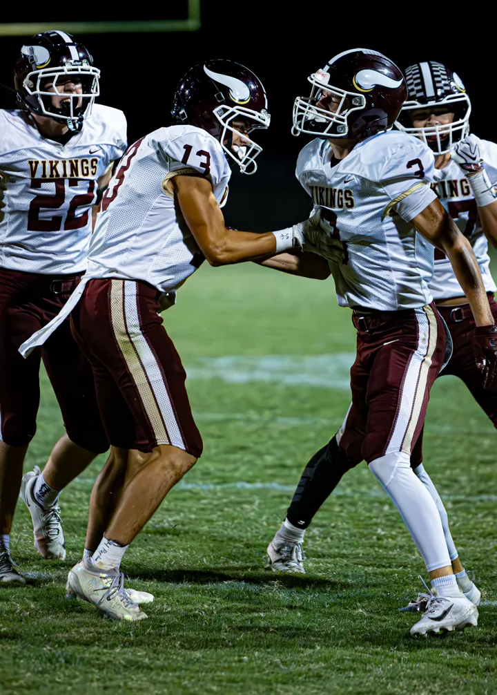 Football teammates in white and maroon move into position during a night game.