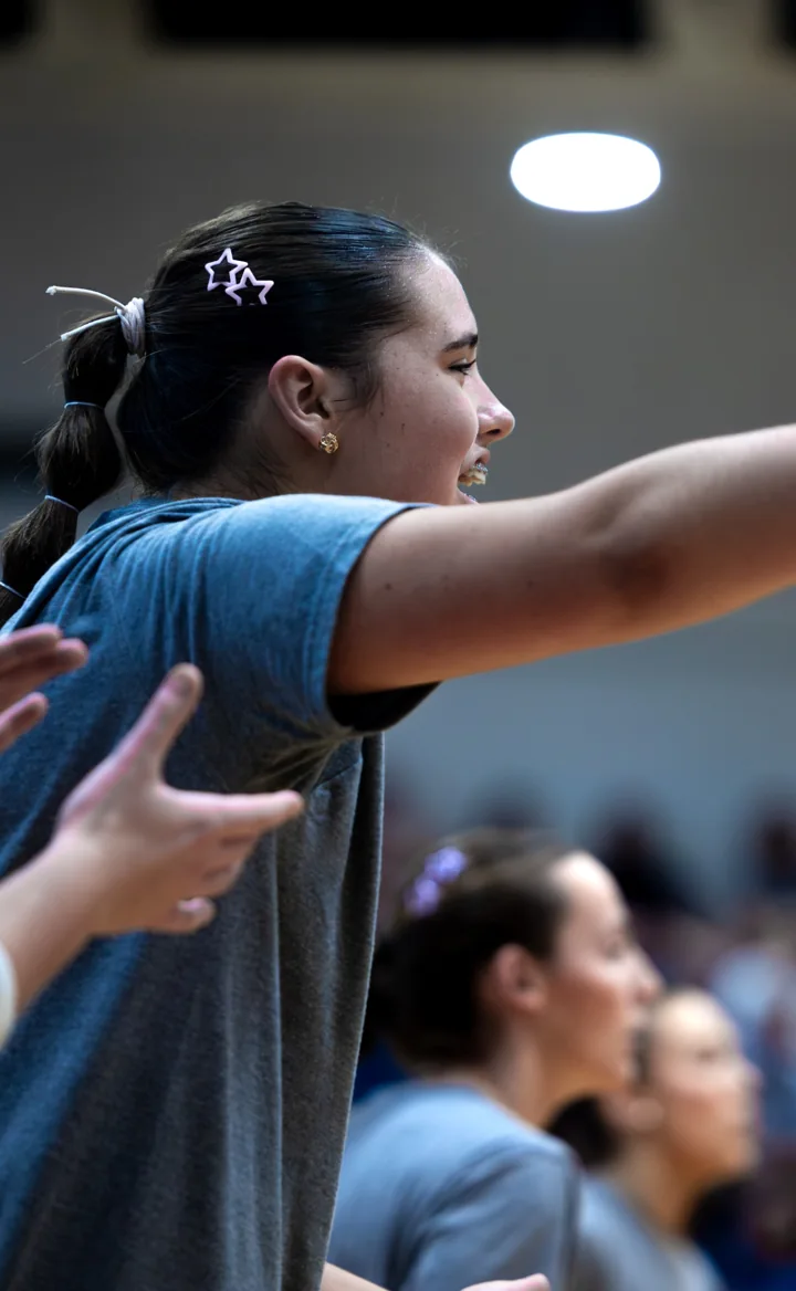 A young woman gestures from the volleyball sideline during a match.