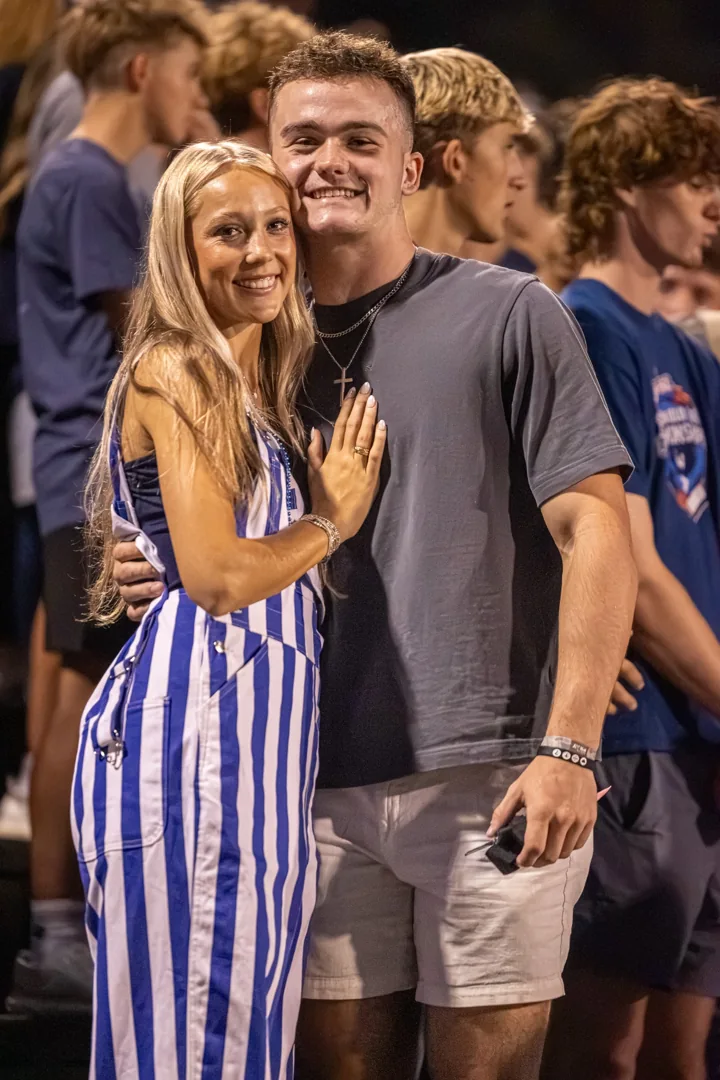 Two smiling people embrace beside the football field.