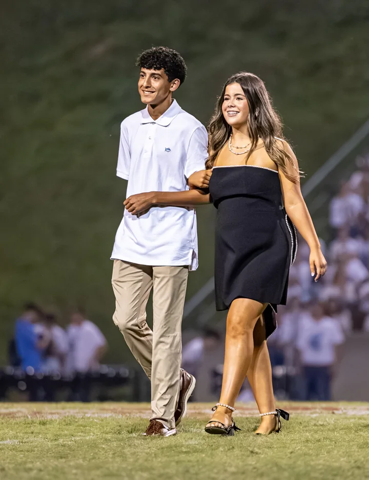 Two people walk arm in arm across a football field dressed for a formal occasion.