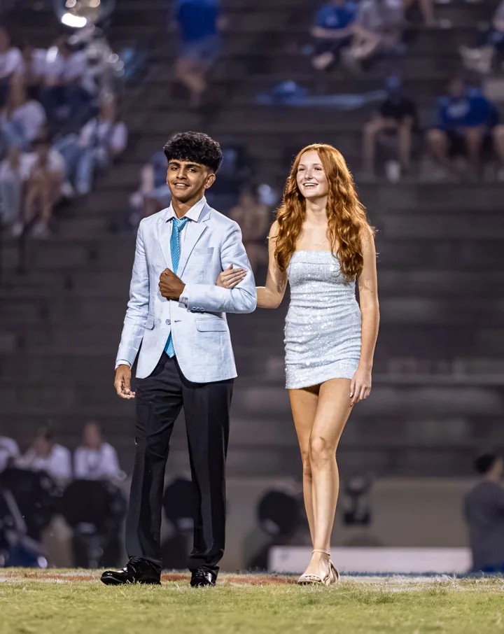 Two people walk together in formal clothes beneath the stadium lights.