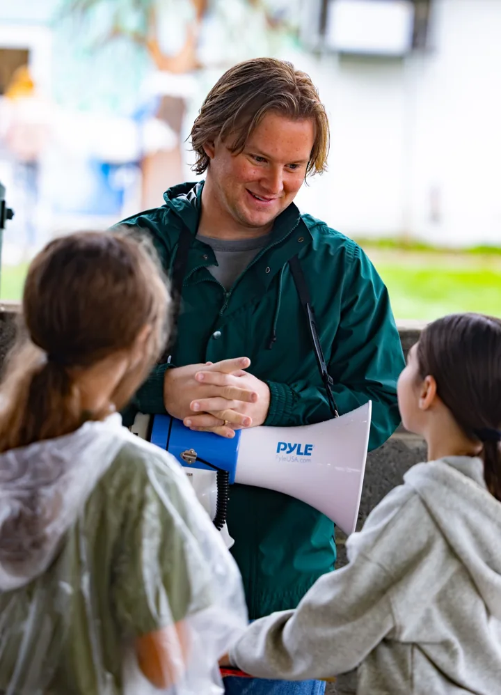 A smiling adult talks with two children during a group activity.
