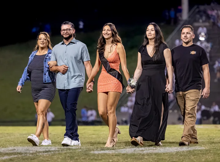 A group of five walks across the football field during a formal recognition ceremony.