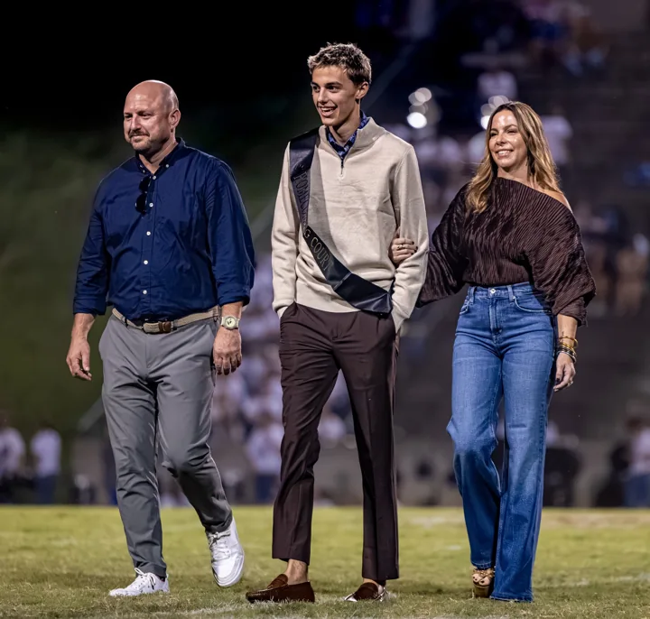 A young man walks across the football field between two adults.
