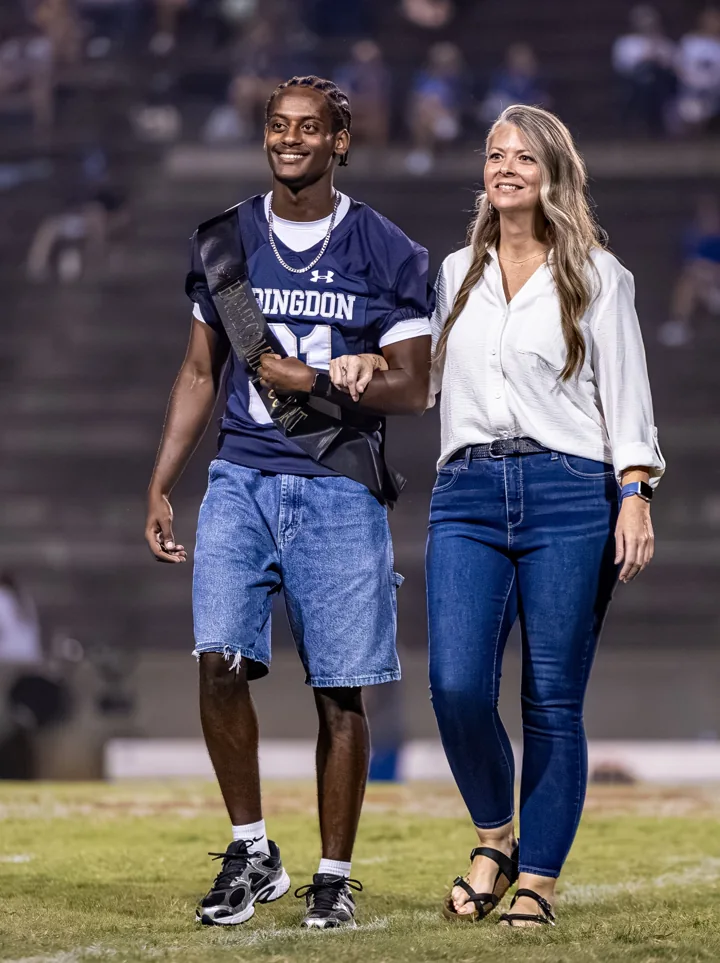 Two smiling people walk arm in arm across the field during a recognition ceremony.