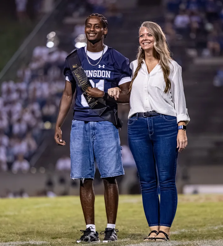 A football player and a companion smile together as they cross the field.