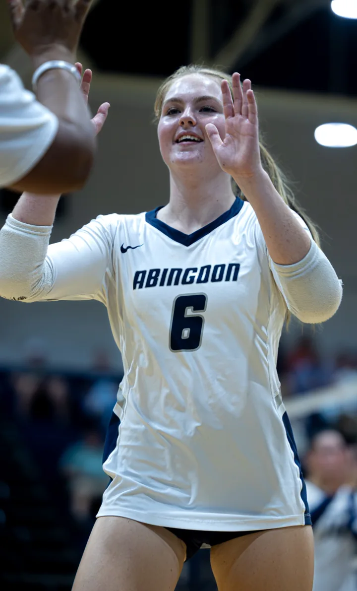 A smiling volleyball player in a white number 6 jersey raises her hands toward a teammate.