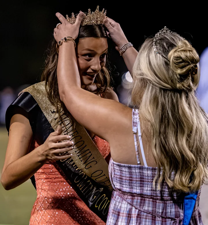 A young woman receives a crown during a ceremony on the football field.