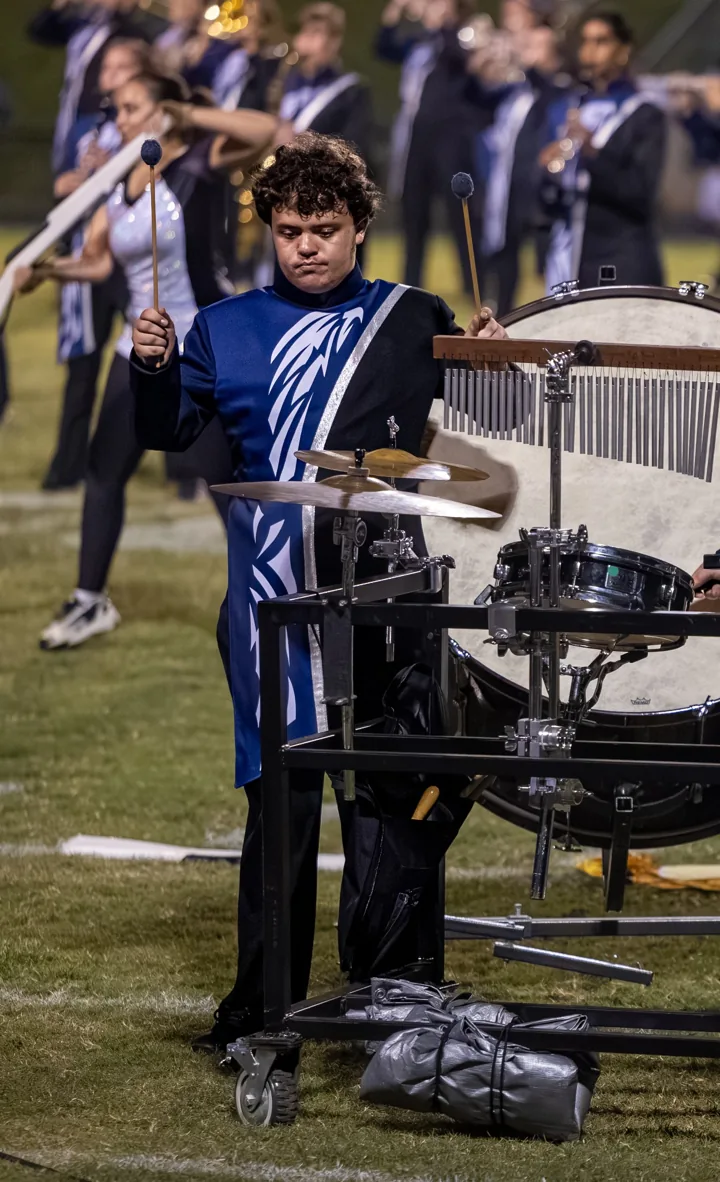 A marching percussionist plays a drum setup on the football field.