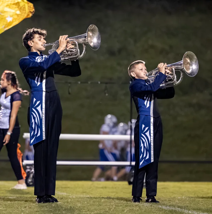 Marching musicians raise their brass instruments during a field performance.