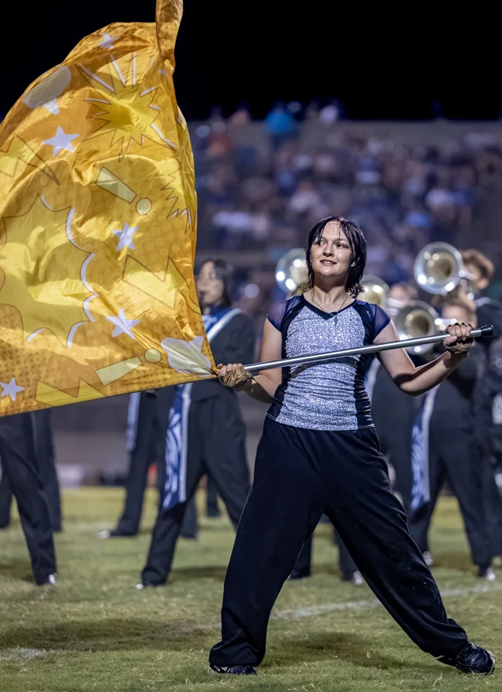 A color guard performer turns with a gold flag during a marching band show.