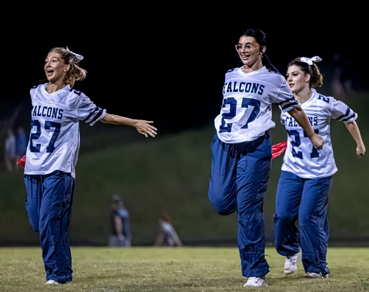 Performers smile and stretch their arms during a routine under stadium lights.