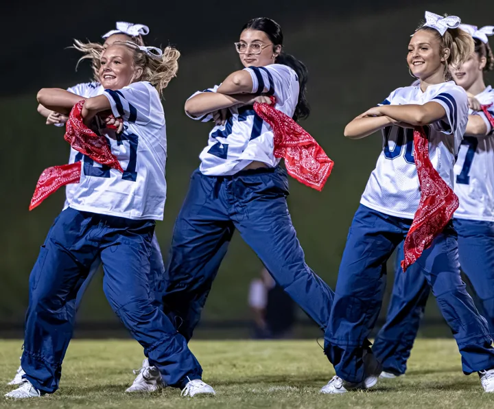 Three performers move in sync with red scarves on the football field.