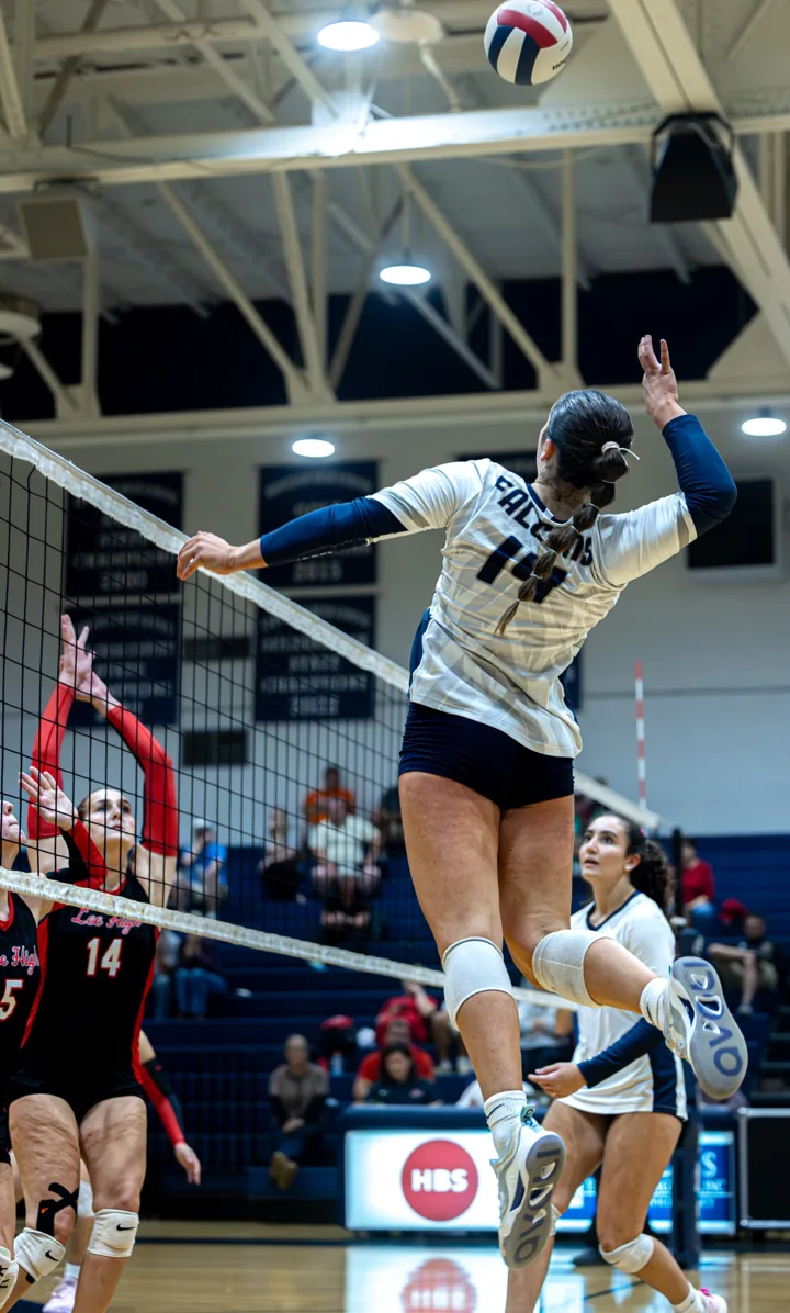 A volleyball player in white swings at the ball while an opponent in red attempts a block.