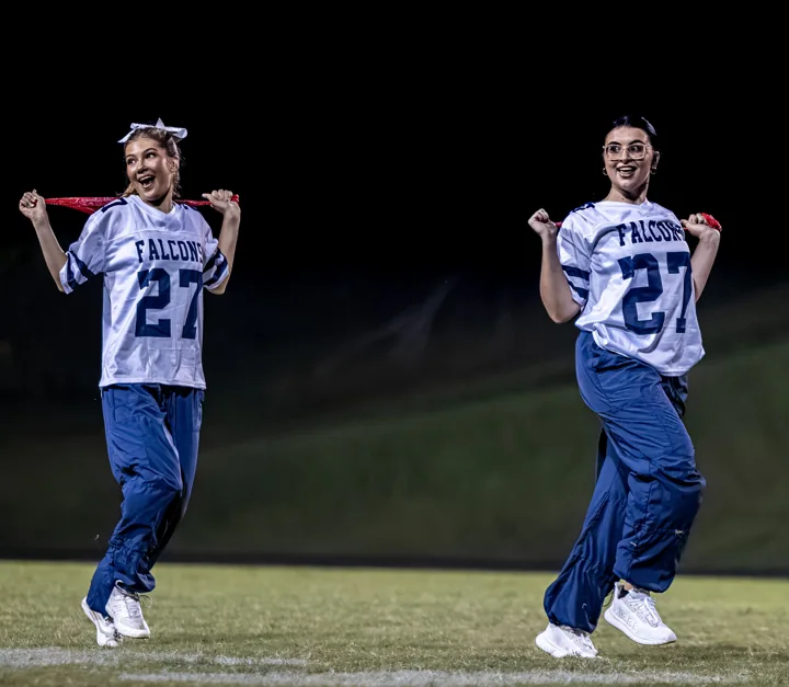 Two performers smile as they move across the field with red scarves.