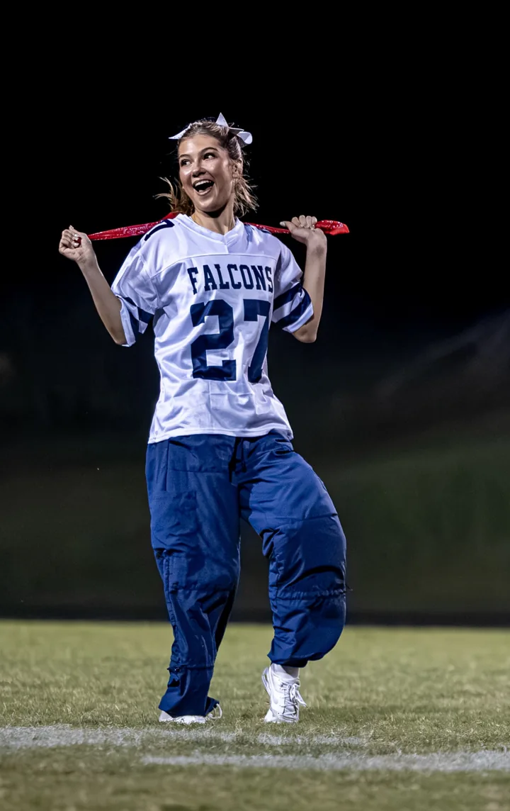 A smiling performer dances in a football-style jersey under stadium lights.