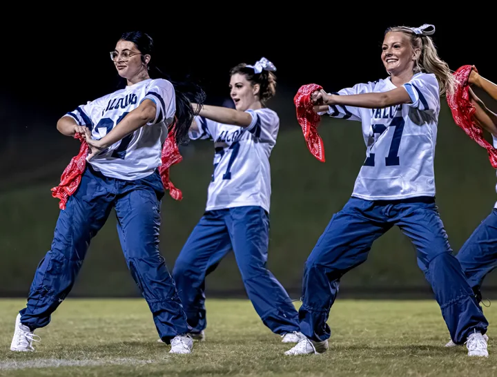 Performers extend their arms together during a coordinated field routine.