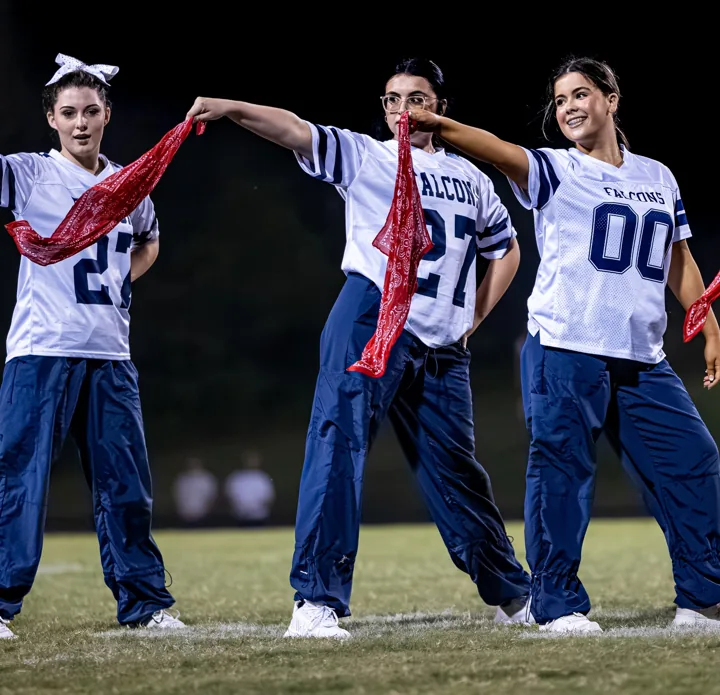Three performers hold red scarves out at the end of a dance movement.