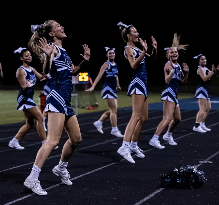 Cheerleaders perform a routine on the track under stadium lights.