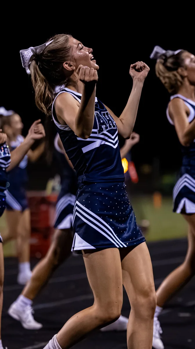 A cheerleader cheers with her arms bent during an evening routine.