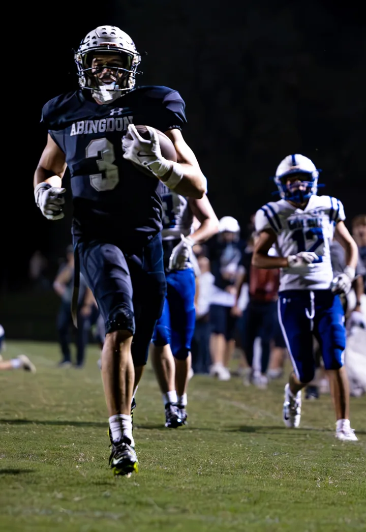 A football player carries the ball toward the camera during a night game.