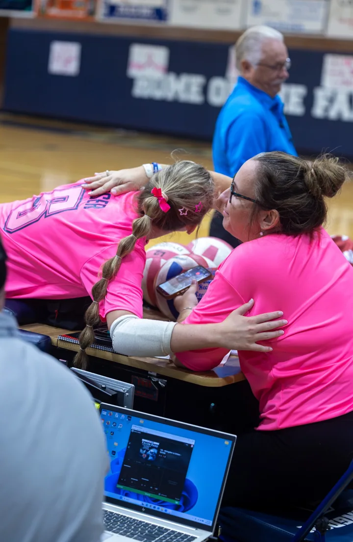 People in bright pink shirts embrace beside the volleyball court.