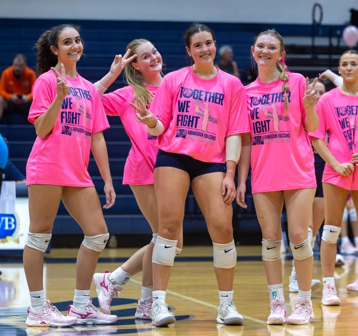 Volleyball teammates in matching bright pink shirts smile together on the court.