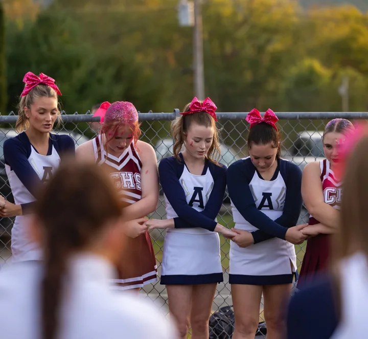 Cheerleaders link arms in an outdoor huddle before a performance.