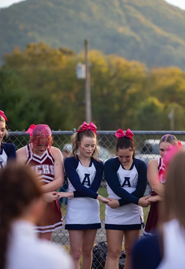 Cheerleaders stand close together with a mountain and autumn trees behind them.
