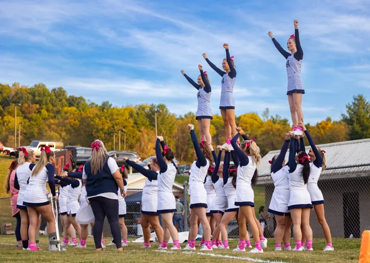 Cheerleaders hold three teammates high in the air beneath a blue autumn sky.