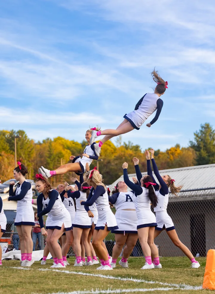 A cheerleader flies above the outstretched hands of her teammates.