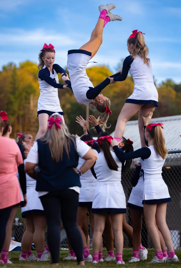 A cheerleader rotates through an airborne stunt as teammates reach to catch her.