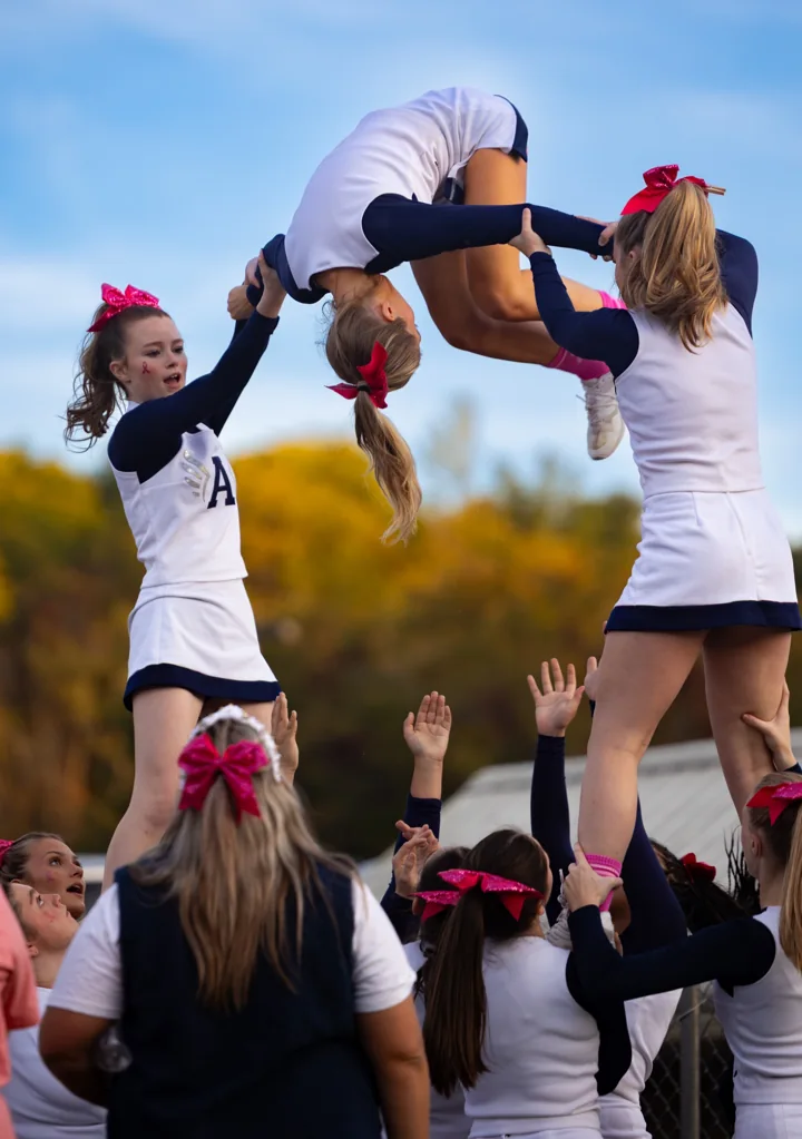A cheerleader folds into a tumbling stunt above teammates ready below.
