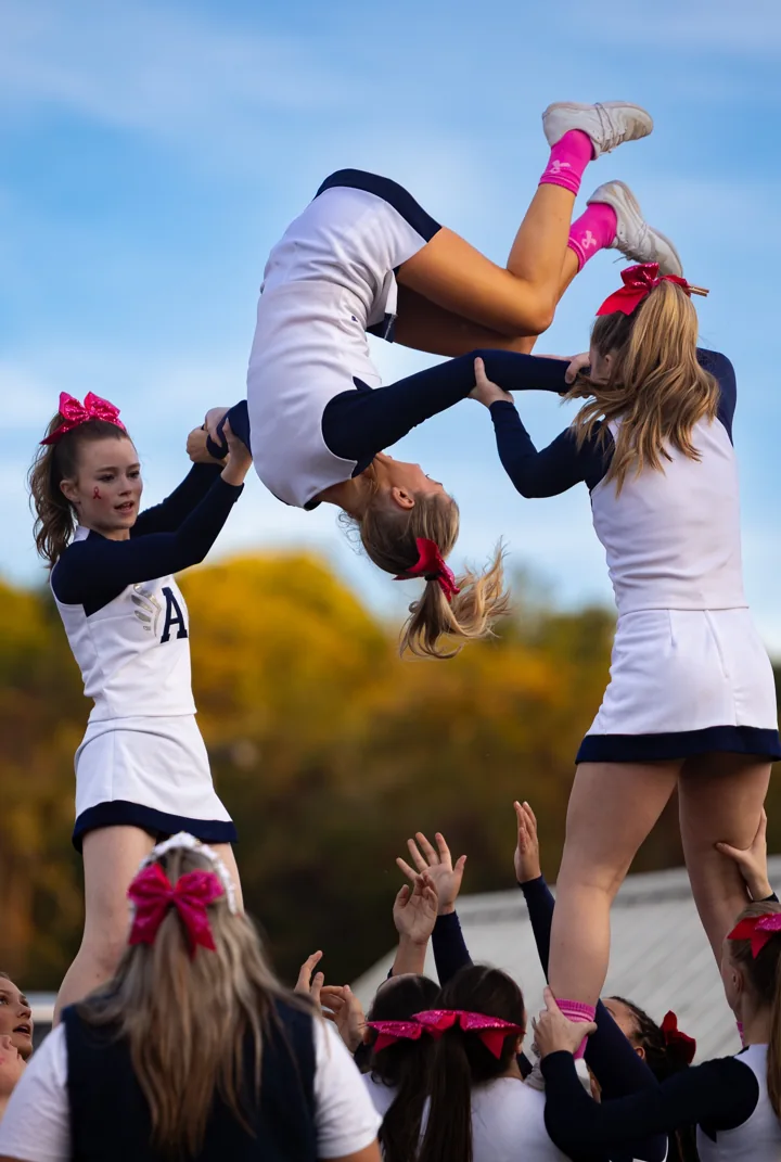 A cheerleader completes an aerial rotation above the hands of her team.