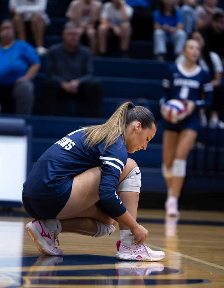 A volleyball player crouches near the court boundary with teammates in the background.