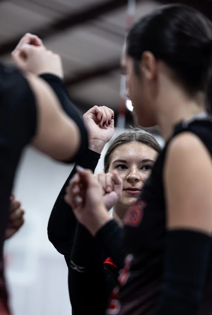 A volleyball player looks toward teammates gathered in a close team huddle.