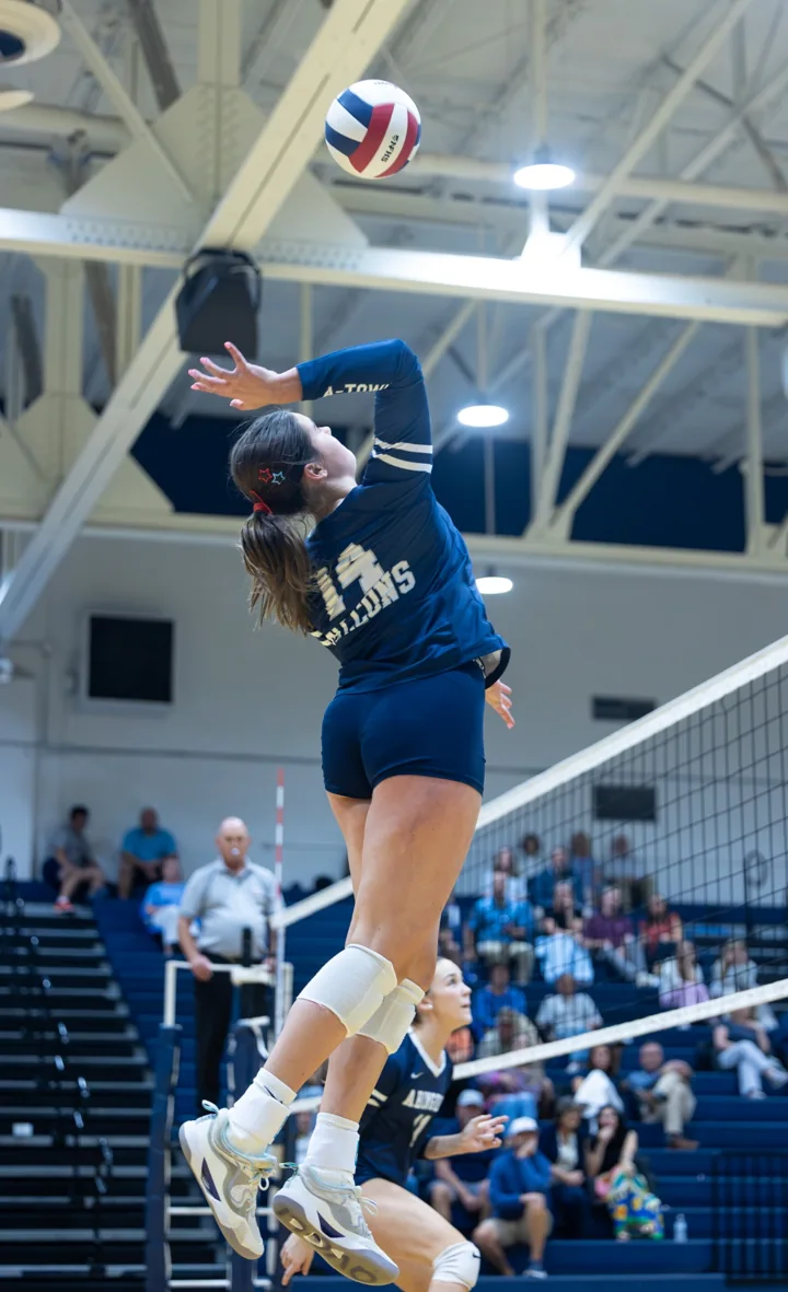 A volleyball player in navy leaps with her arm drawn back to strike the ball.