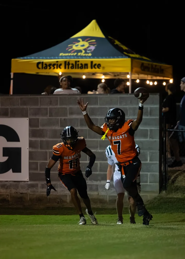 Football players leap with their arms raised near the end of the field during a night game.