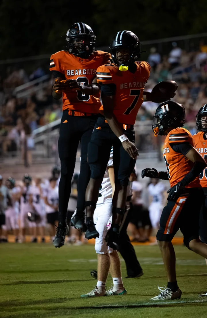 Two football teammates in orange uniforms jump in celebration.