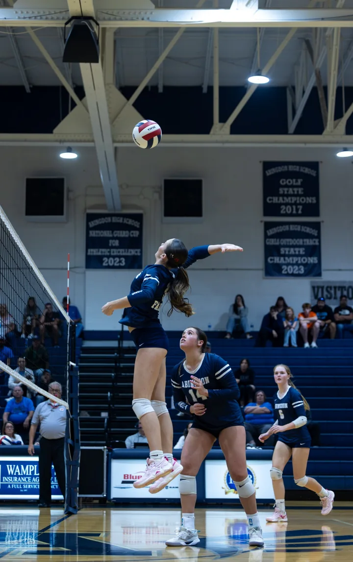 A volleyball player follows the ball overhead with her arm extended for a hit.