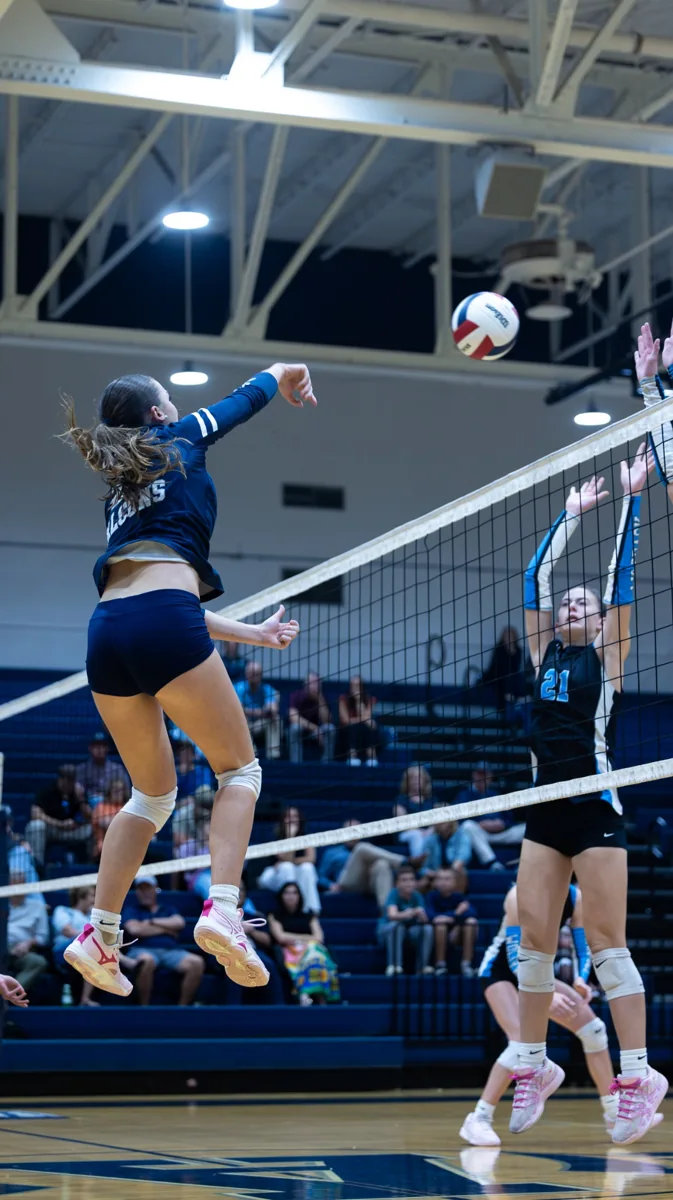 A volleyball player stretches high above the net to strike the ball.