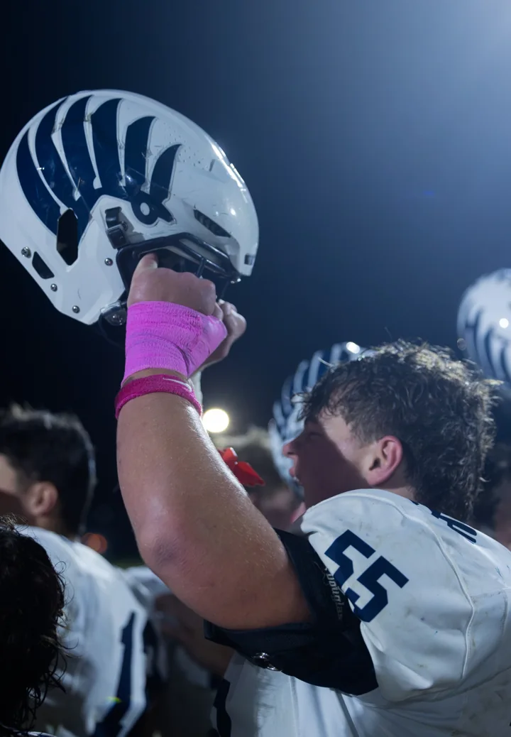A football player raises his helmet beneath stadium lights.
